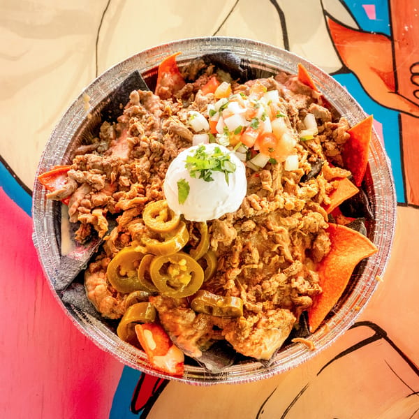 Loaded nachos with ground meat, pico de gallo, sour cream, and jalapeños in a foil container.