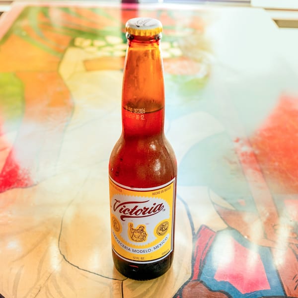 A cold bottle of Victoria beer with condensation, sitting on a colorful, abstract table.