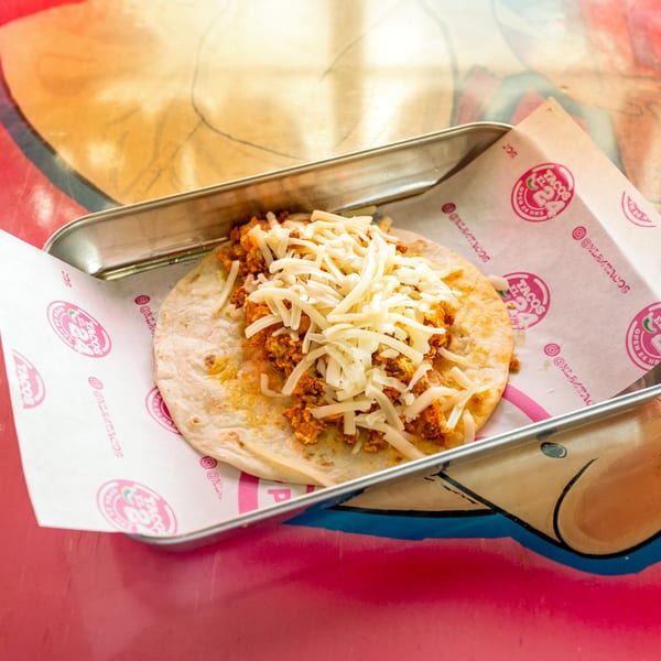 A Tacos El 24 taco with chorizo and shredded cheese on a tortilla, served in a metal tray.