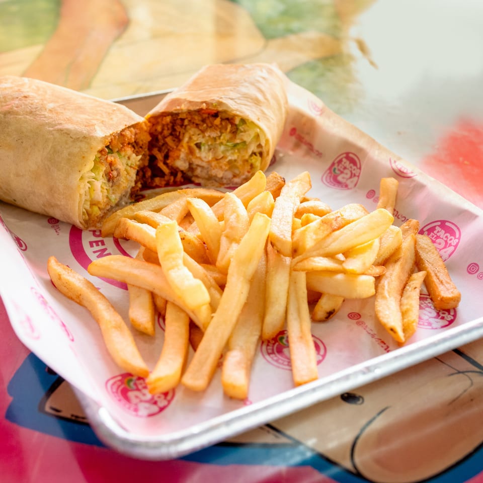A large burrito, cut in half to show the filling, served with a side of golden french fries.