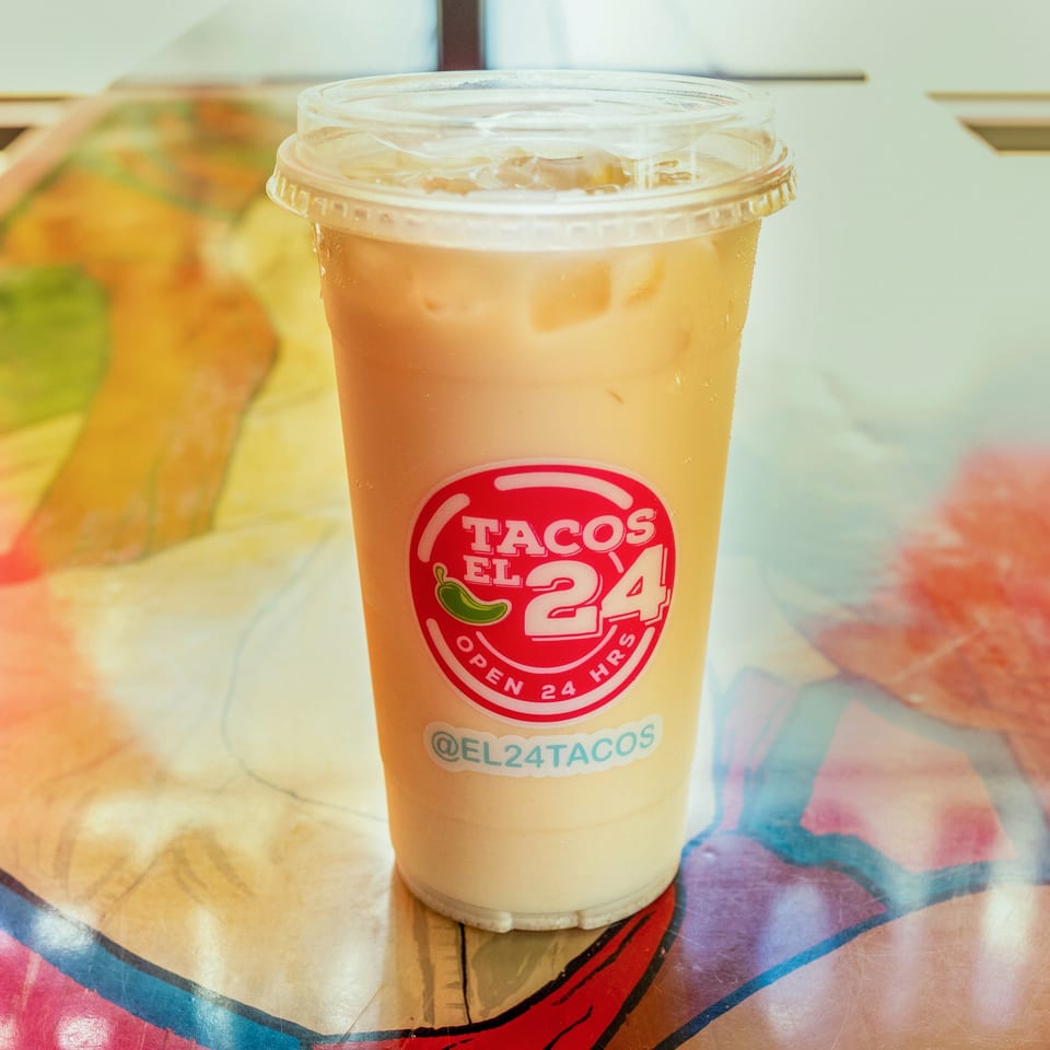 Iced horchata drink from Tacos El 24, with a red logo, on a colorful table.