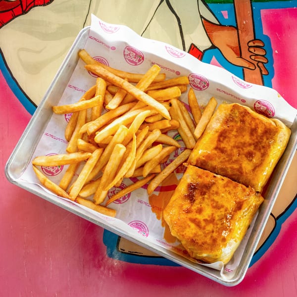 Two golden-brown burritos and a pile of crispy french fries on a metal tray with branded paper.
