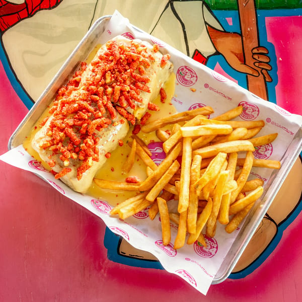 Burrito covered in cheese sauce and red crunchy toppings, served with golden fries on a metal tray.