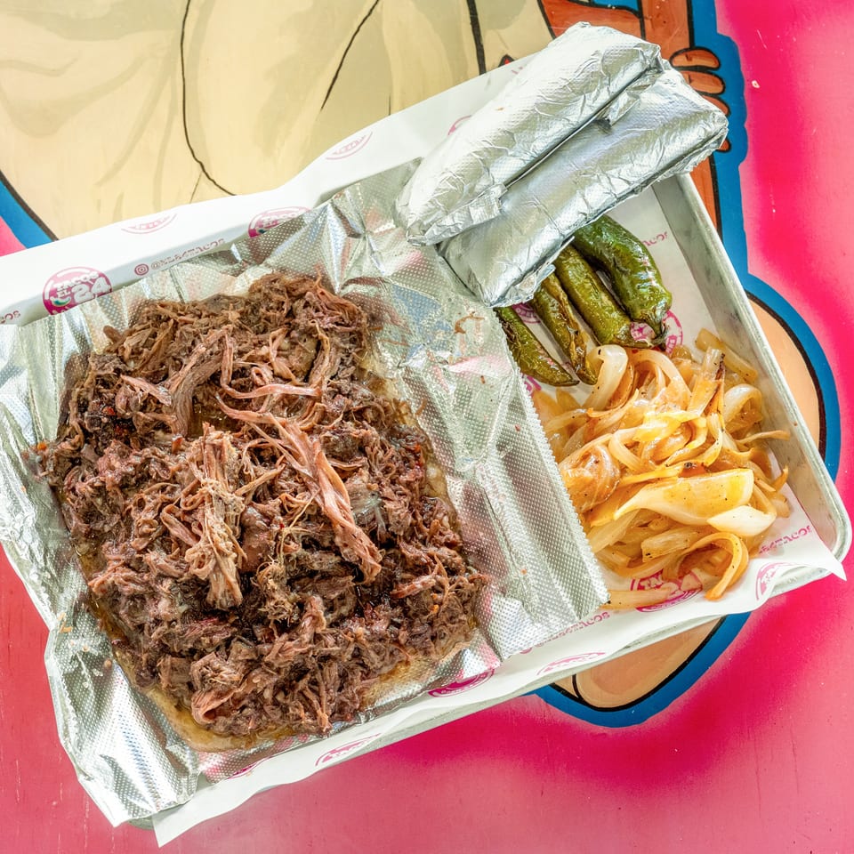 Shredded beef, grilled onions, and green peppers on a foil-lined tray, with two foil-wrapped items.